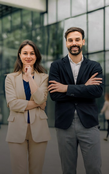 Eine Frau und ein Mann im Business Outfit blicken selbstbewusst in die Kamera.